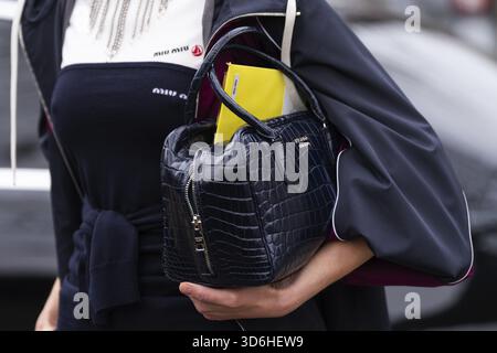 Paris, France - March 11, 2025: Woman wears Prada croc-embossed black leather handbag with gold logo and yellow folder. Fashion blogger outfit details Stock Photo