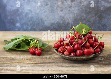 Food, Ripe wet sweet cherries with green leaves in a metal plate on wooden background Stock Photo