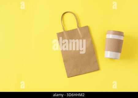 Mockup of kraft paper shopping bag with handles on yellow surface, reusable portable coffee mug for travel. Takeaway mug with spill stopper. Zero wast Stock Photo