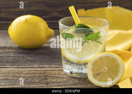Food, Lemonade or mojito cocktail with lemon and mint with ice. Cold summer refreshing drink decorated with yellow napkin on wooden background Stock Photo