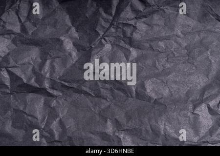 Dark wrinkled creased black paper poster texture. Blank crumpled grainy paper textured surface. Smudged grungy cardboard with fiber. Close up. Materia Stock Photo