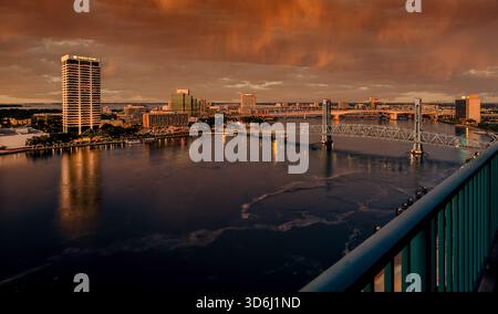 Downtown Jacksonville glows beneath rolling orange storm clouds as the St. Johns River reflects the shifting light of a dramatic morning sky. Stock Photo