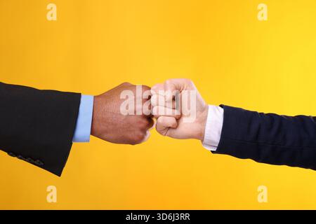 African American man bumping fists with his business partner on yellow background, closeup Stock Photo