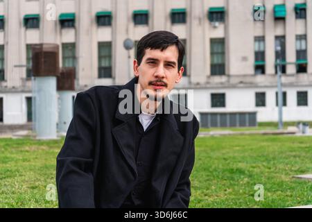 Young man wearing a black coat in an urban outdoor environment, looking directly at the viewer with a serious expression Stock Photo