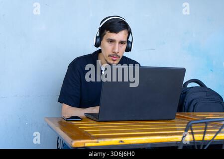 Focused student working remotely on laptop with headphones, engaging in distance learning or a online job Stock Photo