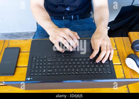 Man's hands actively typing on a laptop keyboard, using a trackpad, working remotely from a wooden desk Stock Photo