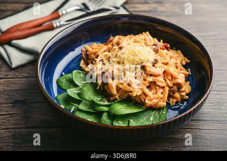Close-up of Orzo pasta with sun-dried tomato,  chicken hard cheese and spinach on dark wooden background Stock Photo