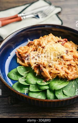 Close-up of Orzo pasta with sun-dried tomato,  chicken hard cheese and spinach on dark wooden background Stock Photo