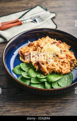 Close-up of Orzo pasta with sun-dried tomato,  chicken hard cheese and spinach on dark wooden background Stock Photo