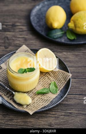 Homemade lemon curd in a glass jar with mint leaves and fresh lemons on a wooden background Stock Photo