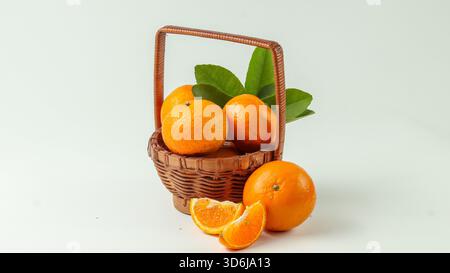 some sweet and fresh mandarin oranges in a rattan basket and one orange and orange slices are outside the basket on a white background Stock Photo
