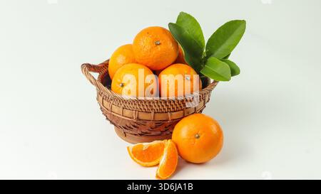 some sweet and fresh mandarin oranges in a rattan basket and one orange and orange slices are outside the basket on a white background Stock Photo