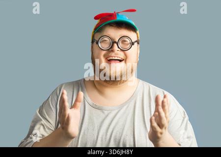 Laughing chubby man in propeller beanie and round glasses, clapping hands, studio Stock Photo