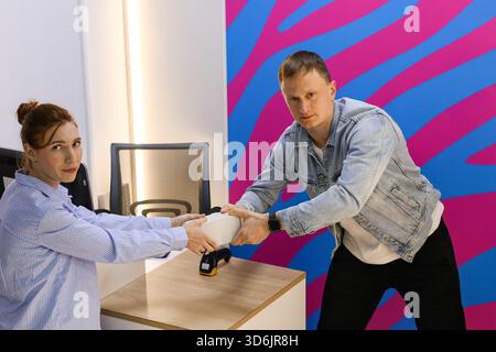 Woman behind counter and man in front pull small white box in tug-of-war style Stock Photo