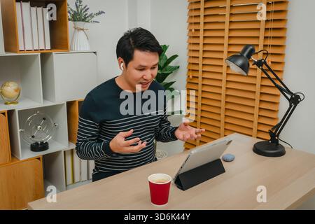 stressed young man using digital tablet and wireless earbuds making video call in home office Stock Photo