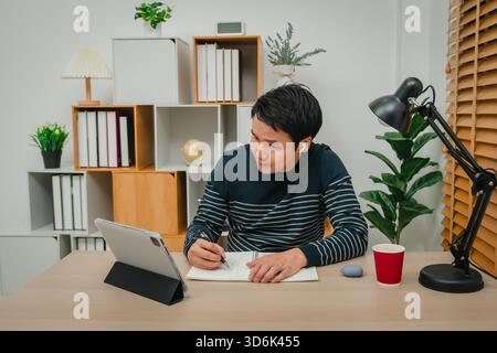 young man learning online with tablet and wireless earbuds at home office Stock Photo