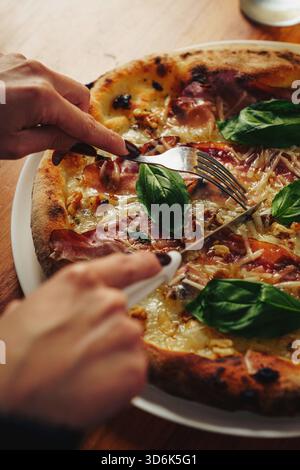Two gourmet pizzas topped with pork, cheese, vegetables and herbs in open boxes with a fizzy drink on a wooden table, overhead view. Stock Photo