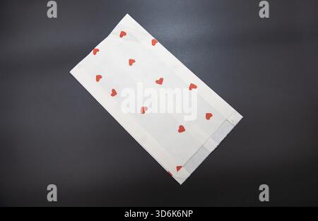 White paper gift bag with small red heart pattern on dark background for celebration Stock Photo