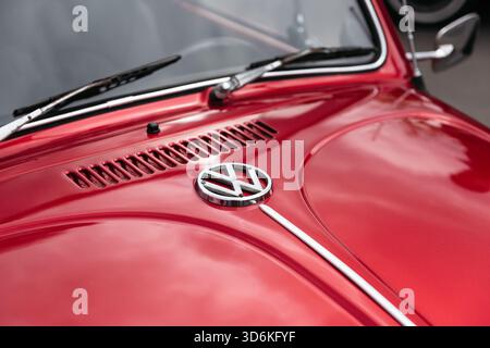 Emblem near the windshield of old VW Beetle. Shiny chrome emblem on the front trunk of red 1960s Volkswagen bug. Stock Photo