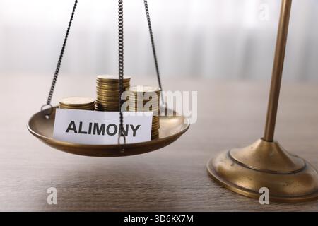 Paper note with word Alimony, scales and coins on wooden table, closeup Stock Photo