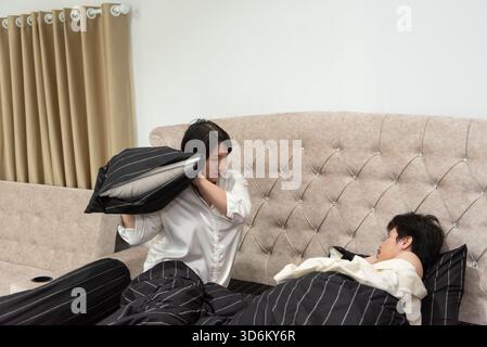 Two LGBTQ friends in bed cleaning their home in the morning. A man with long hair and a short-haired woman engage in daily routine activities with a p Stock Photo