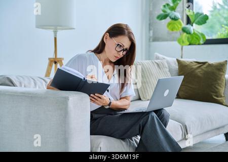Middle aged serious woman working on c with laptop notepad Stock Photo