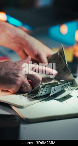 Hands Counting Polish Zloty Banknotes. Close-up male hands quickly sorting thick stack 100 PLN bills above notebook at modern office desk under warm a Stock Photo