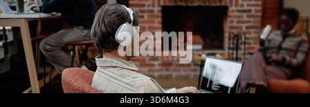 Header of Young Caucasian Man in Headphones Coding on Laptop near Fireplace Stock Photo