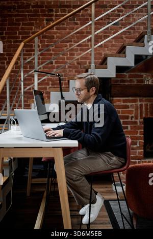 Caucasian Young Adult Man Working on Laptop in Modern Business Office Setting Stock Photo