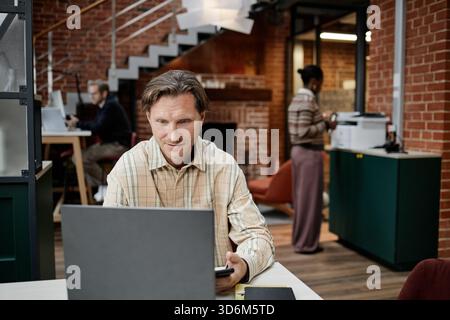 Caucasian Middle Aged Man Using Laptop While Colleagues Working in Office Stock Photo