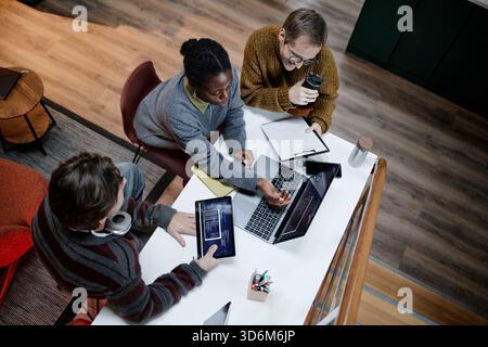 Diverse Young Adults Collaborating on Project Using Laptop in Modern Office Stock Photo
