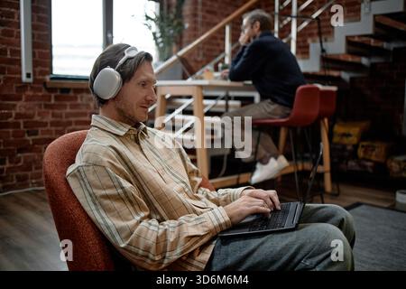 Young Caucasian Man Using Laptop and Wearing Headphones in Modern Office Stock Photo