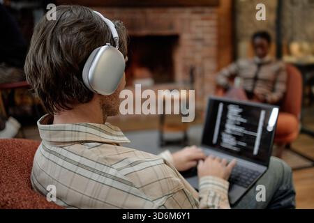 Young Adult Caucasian Man Using Laptop and Listening to Music in Modern Office Stock Photo