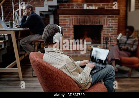 Young Caucasian Man Wearing Headphones Working on Laptop in Modern Office Stock Photo