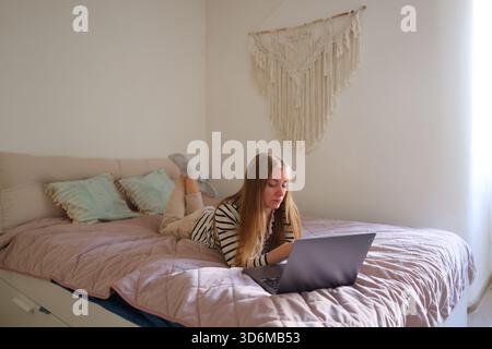 Happy woman enjoying remote work or studying online in cozy bedroom setting. Stock Photo