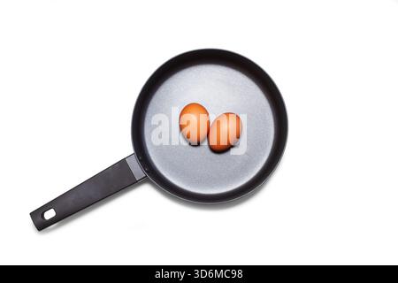 A black frying pan with two eggs inside in a top view on a white background with copy space Stock Photo
