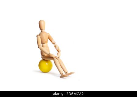 A wooden mannequin sitting on a yellow ball isolated on a white background with copy space Stock Photo