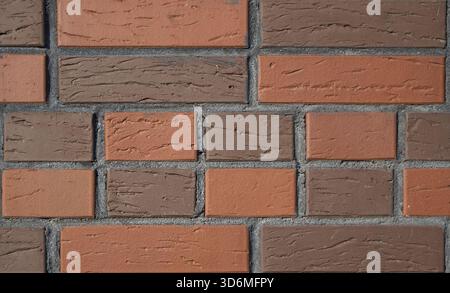 Close up view of brick wall features alternating pattern of red orange and brown bricks. The surface has rough, textured appearance with distinct mort Stock Photo
