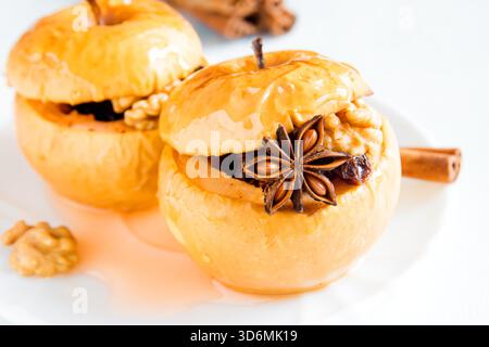 baked apples stuffed with dried fruit, nuts, cinnamon, anise and honey on white plate close up Stock Photo