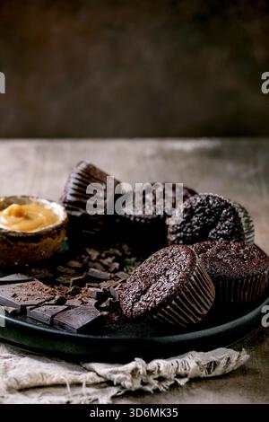 Homemade chocolate cupcakes muffins with salted caramel sauce and chopped dark chocolate on black ceramic plate over concrete texture background. Stock Photo