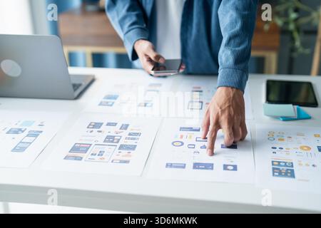 UX UI Designer Planning innovative Mobile App with Paper Wireframe Designs at Workspace || Model released Stock Photo