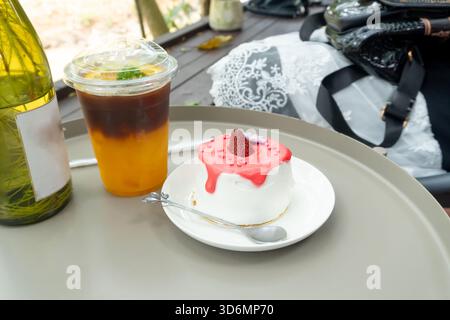 Iced lemon tea in transparent plastic glass and strawberry cake with glazed cream in mini white plate with mini silver spoon or tea spoon are served t Stock Photo
