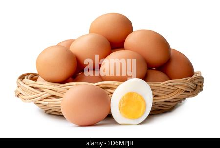 Many raw brown chicken eggs with boiled eggs and egg yolk in a half in stack in wicker basket are isolated on white background with clipping path. Stock Photo