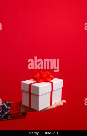 White holiday gift box with a red ribbon held on a child’s hand against a clean bright red festive background Stock Photo