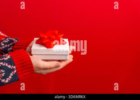 Two hands holding a white gift box with a red bow on a vivid red background, suitable for seasonal branding and festive marketing materials Stock Photo