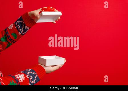 Hands opening a white gift box with red bow on a clean red background, perfect for holiday visuals, copyspace layouts, and seasonal campaigns Stock Photo