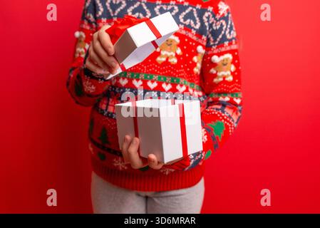 Child opening a white gift box with red ribbon on a bright red background, ideal for festive ads, holiday messaging, and seasonal branding Stock Photo