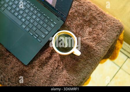 Overhead close-up of coffee cup next to laptop keyboard Stock Photo