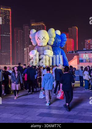 Changsha IFS Tower rooftop plaza illuminated at night, featuring large KAWS Companion sculptures and a crowd of people. Iconic urban art installation Stock Photo