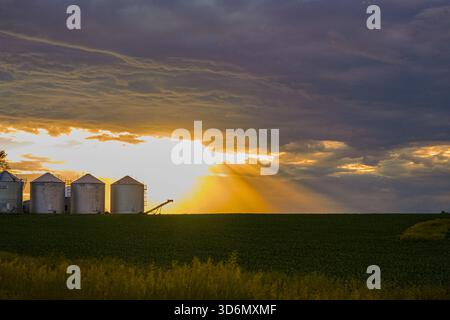 Sun Rays Shining Through Clouds Behind Grain Bins Stock Photo